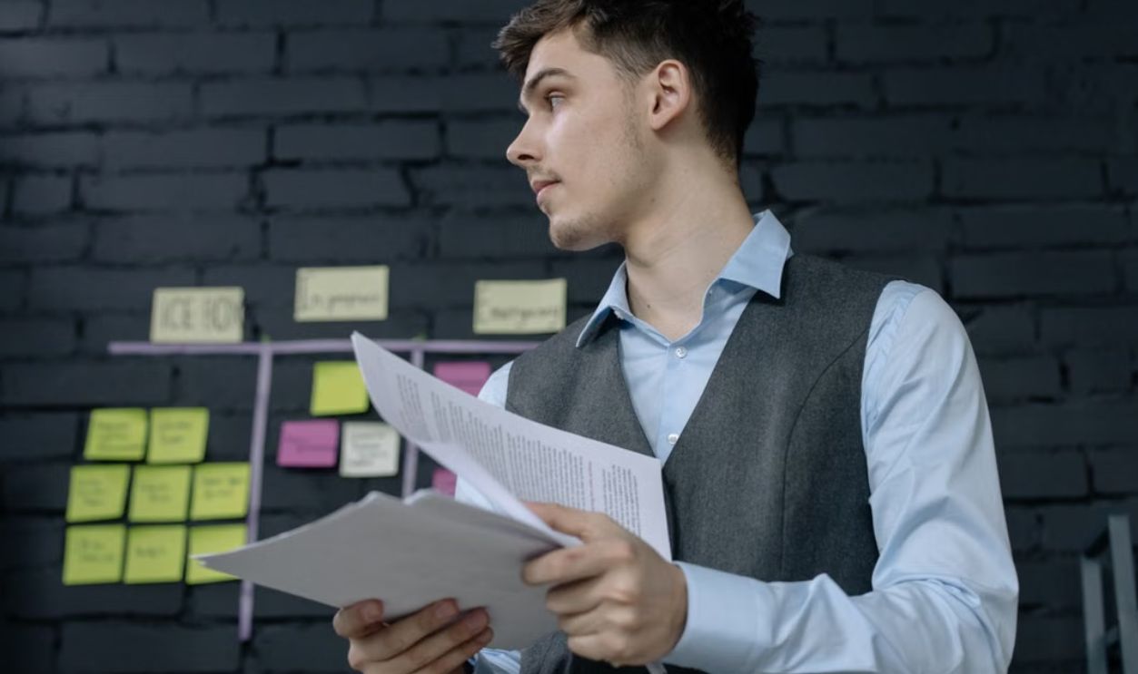 Young male professional analyzing project documents in a modern office setting with a task board