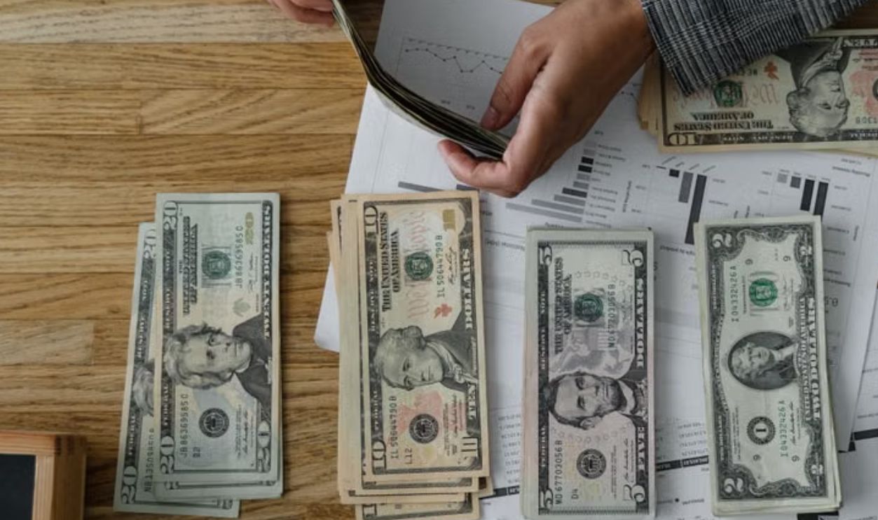 Person counting cash with a calculator and documents on a wooden desk, representing financial planning.