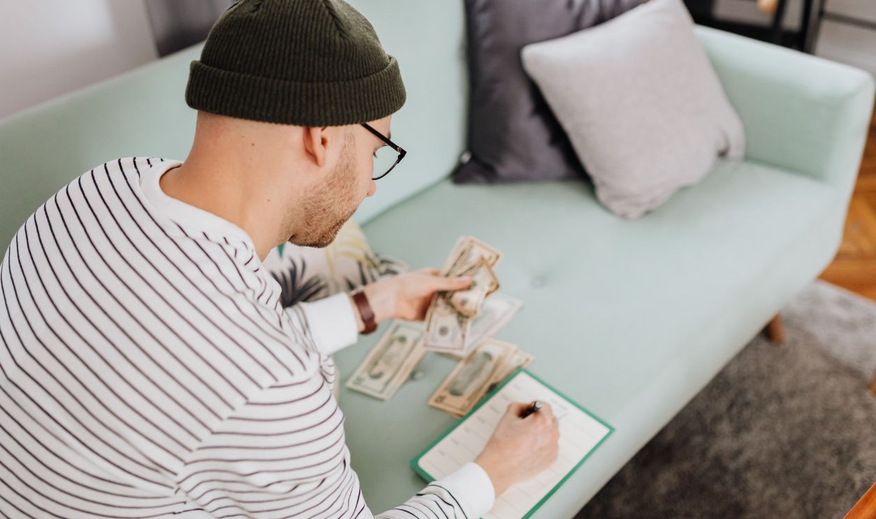 Caucasian man counting money and writing notes while sitting indoors on a couch