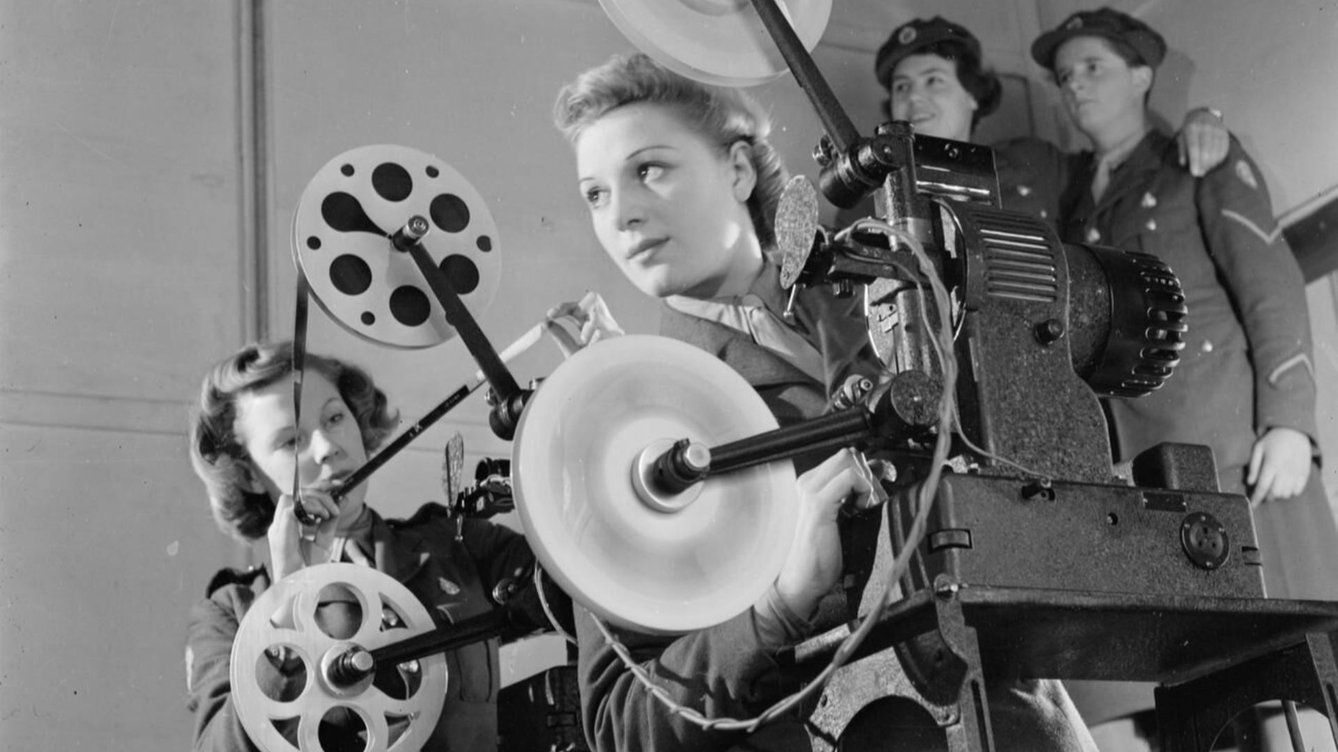 Ats Cine Projector Operators, Aldershot, Hampshire, England, UK, 1941
Two cine projectionists of the Auxiliary Territorial Service operate a 16mm De Vry Simplex Ampro projector at the field stores, Aldershot.  Behind them, two more ATS girls stand in the 