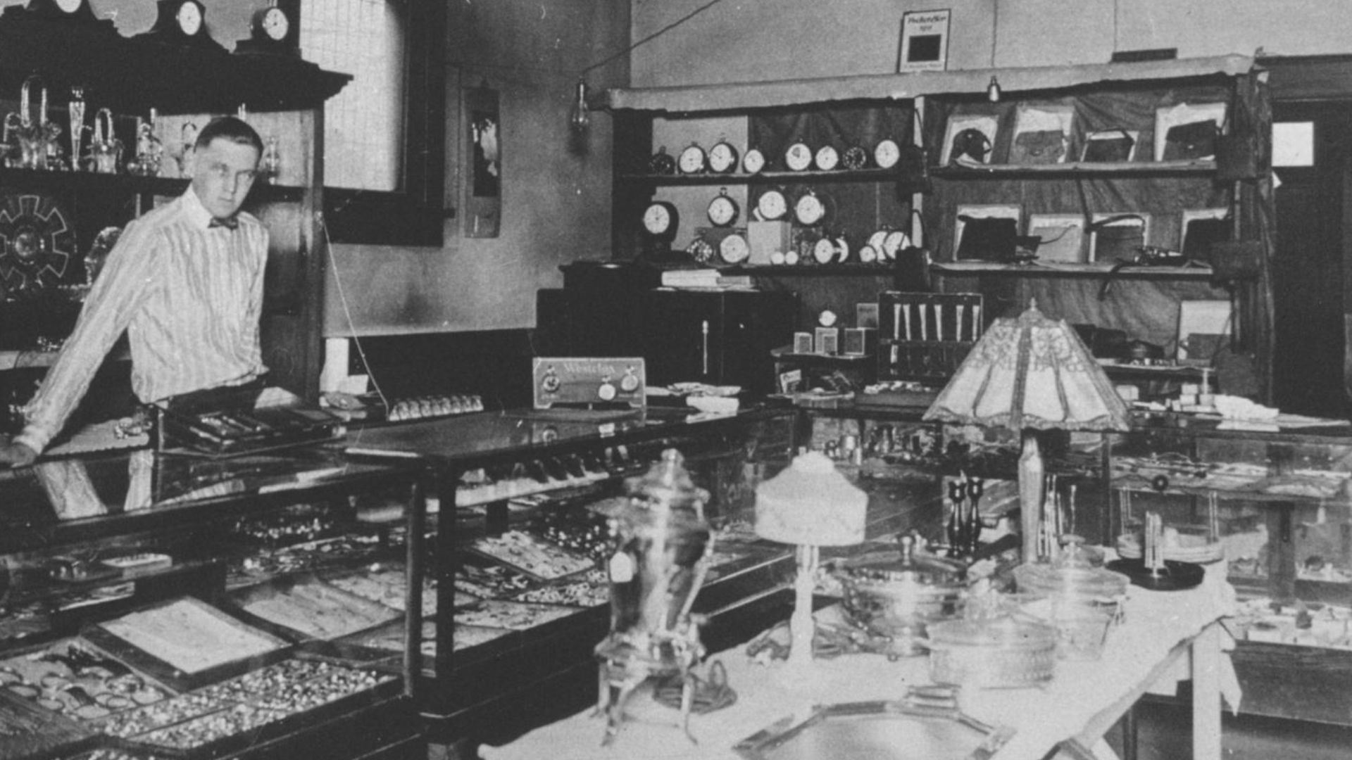 A man stands behind the counter of a jewelry store in Carbon County, Utah. Original image and information can be found at the Utah Department of Heritage & Arts digital collections or the Utah State Historical Society.