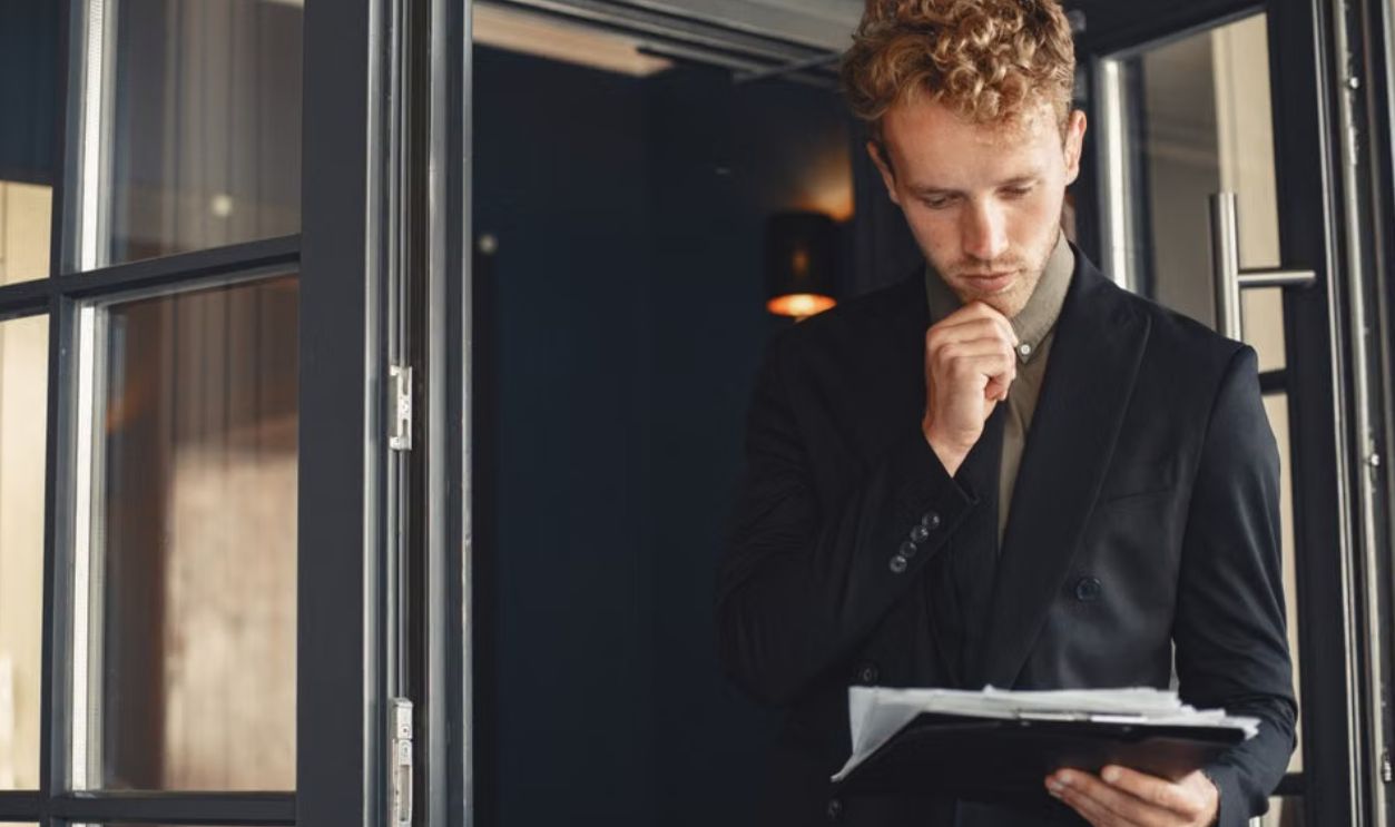 A businessman in a suit thoughtfully reviews documents while standing by a door outdoors