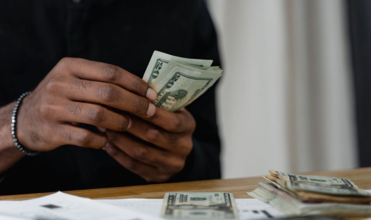 Adult counting dollar bills at a desk, focused on money management and finance
