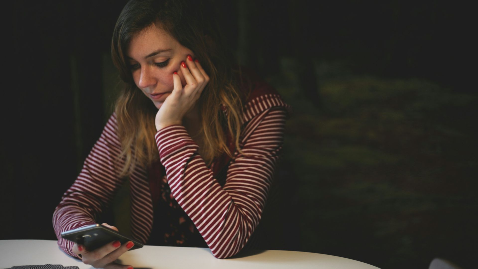 woman leaning on white wooden table while holding black Android smartphone