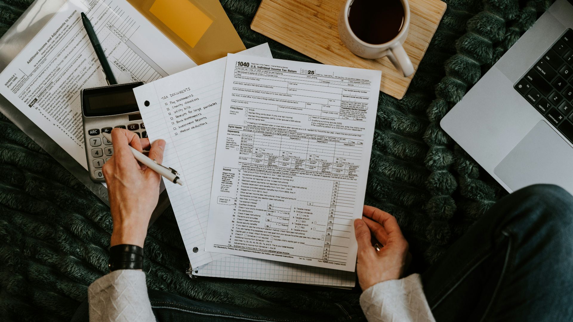 Person reviewing documents with calculator and laptop.