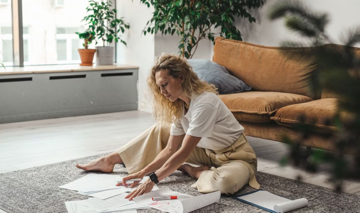 A woman sitting on the floor of her living room working on documents and papers, embodying a comfortable work-from-home atmosphere