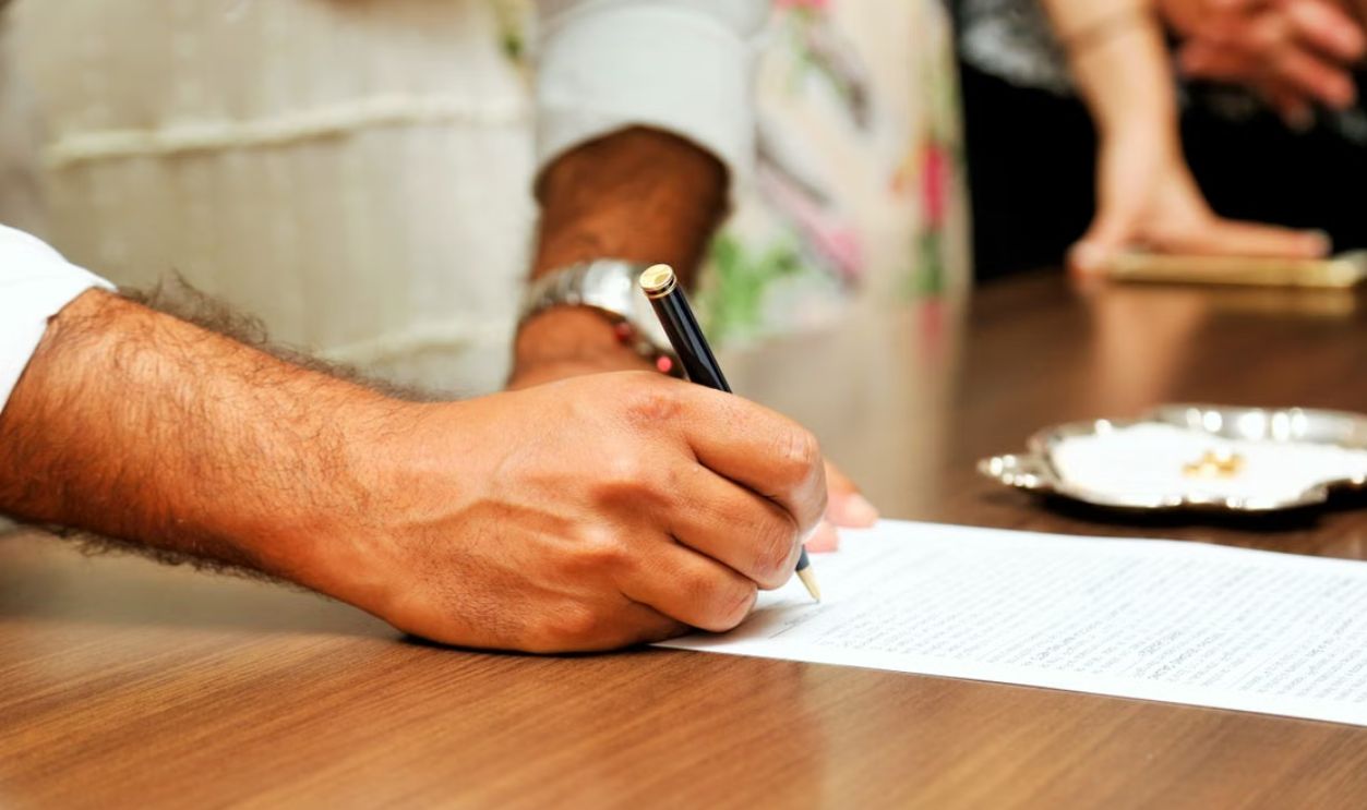 Close-up view of a person signing an important document with a pen on a wooden table