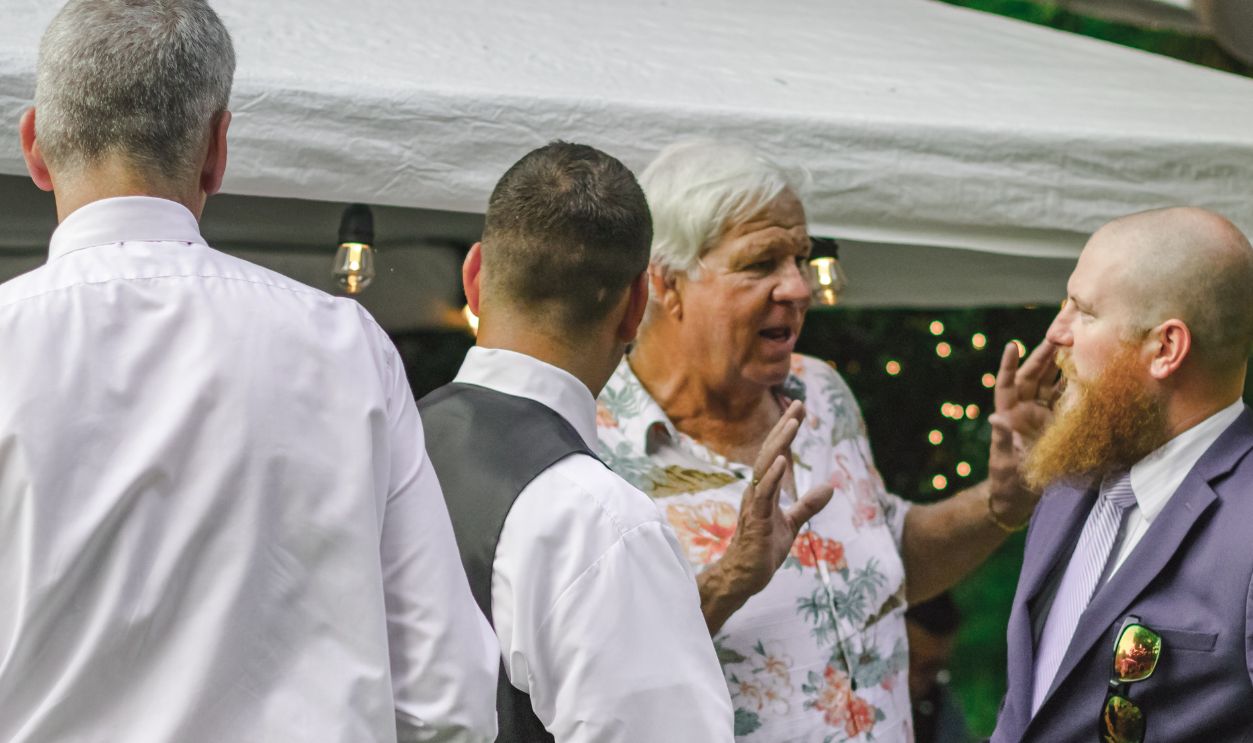 A group of men in conversation at an outdoor event with festive lighting