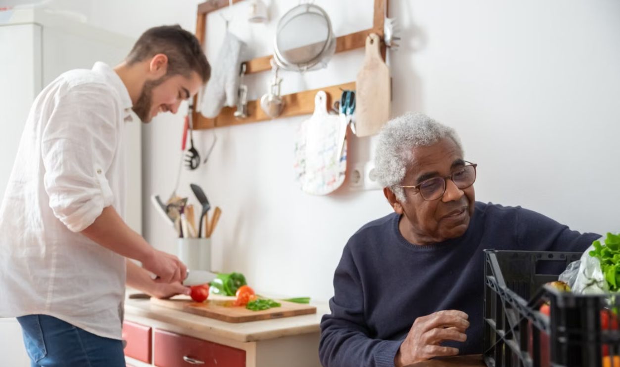 A senior man and young man preparing vegetables together in a cozy kitchen setting.