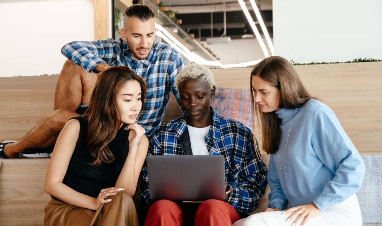 A diverse group of young adults collaborating on a laptop indoors, showcasing teamwork