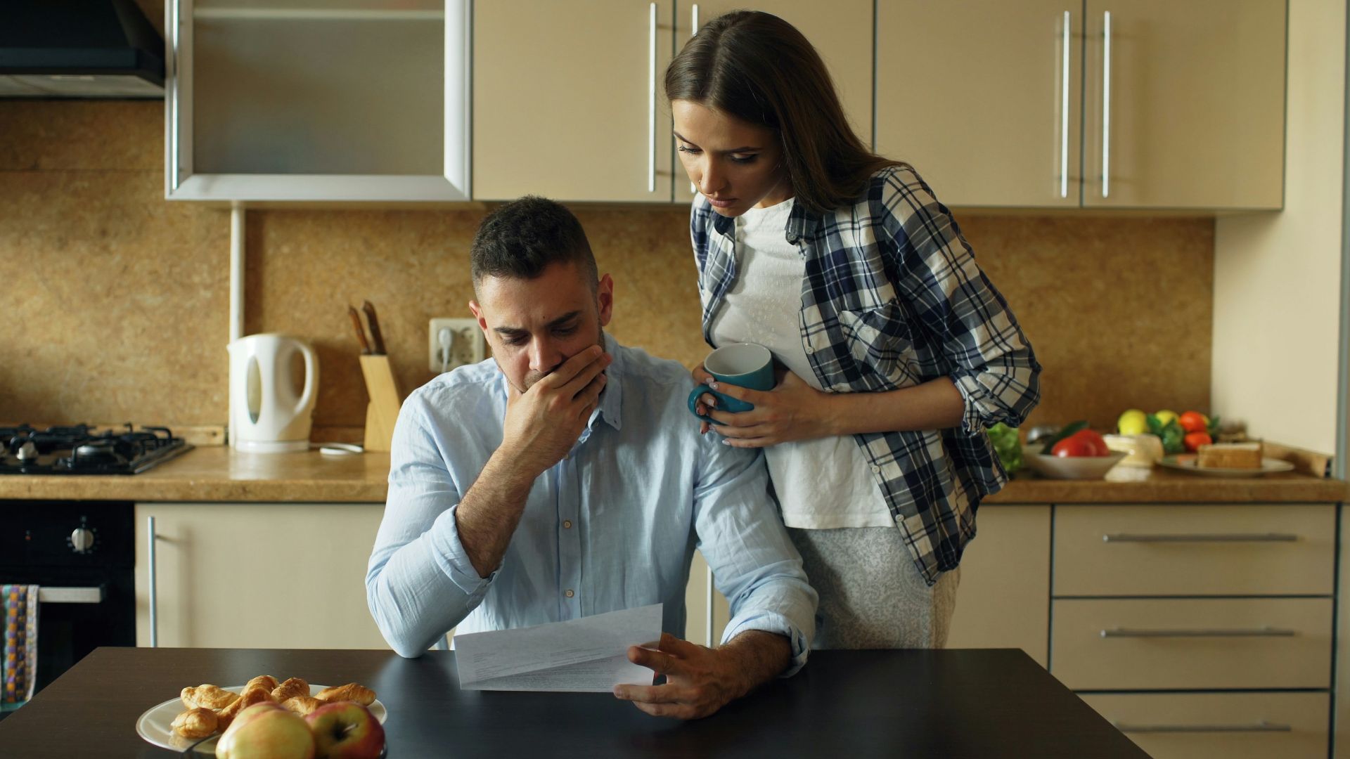 Couple looking stressed over bills at kitchen table.