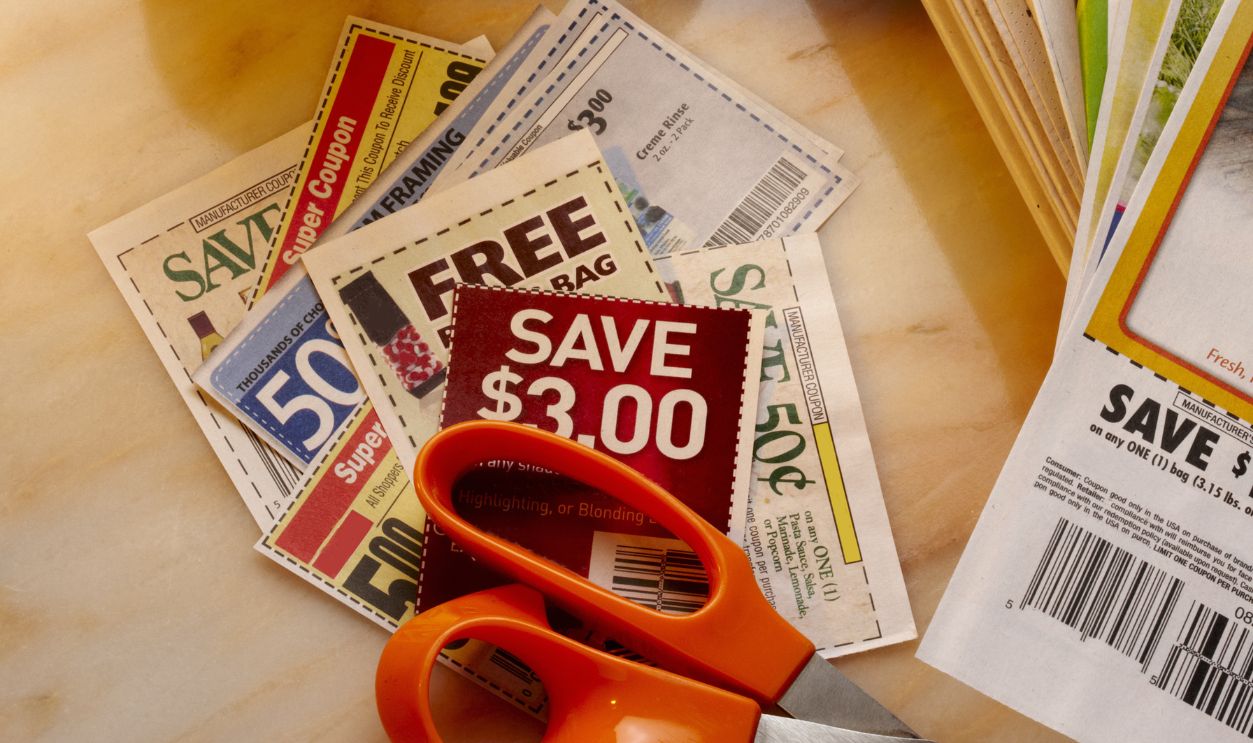 Savings coupons, newspapers, a pair of scissors and a cup of coffee shot on marble table
