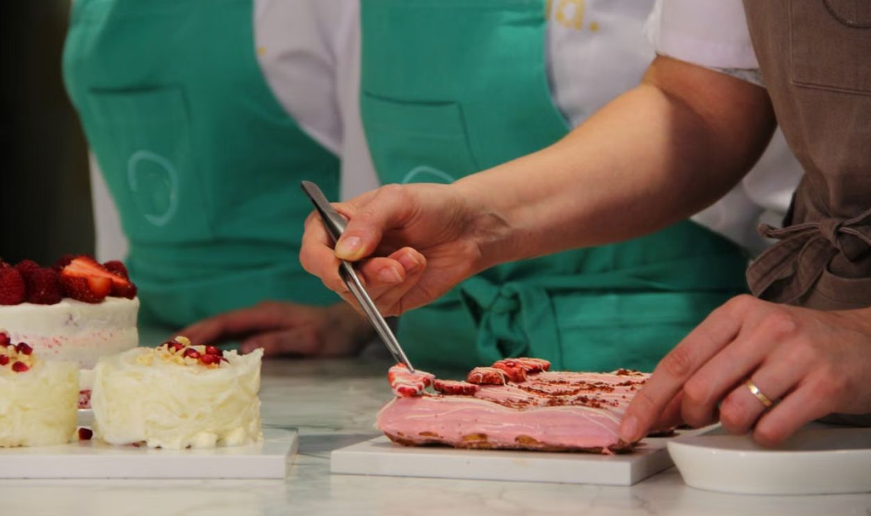 Close-up of pastry chefs in aprons meticulously decorating gourmet cakes with precision and artistry