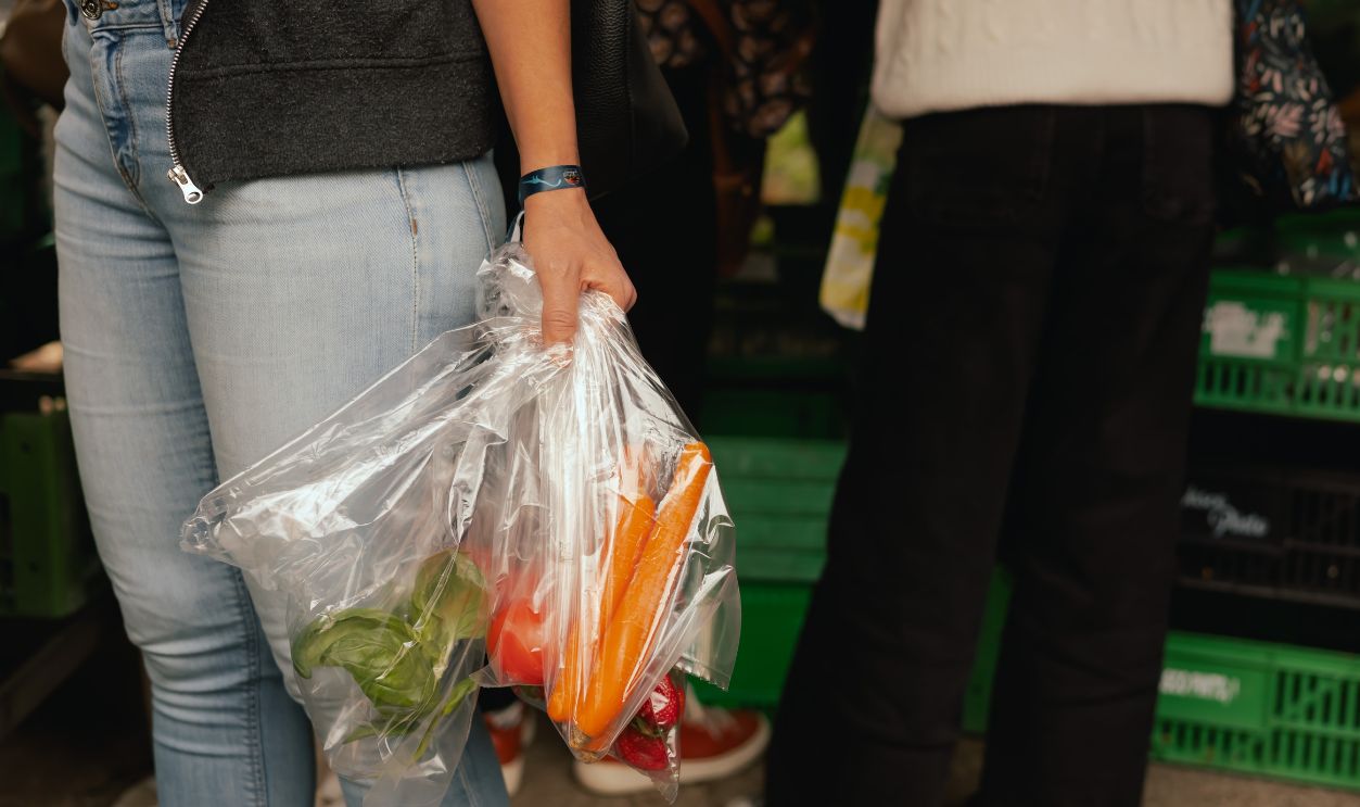 Close up of hand with a vegetables and greens in polyethylene bag on the local Farmers market. Mature Female Customer Shopping At Farmers Market Stall. Close up. Part of the series.