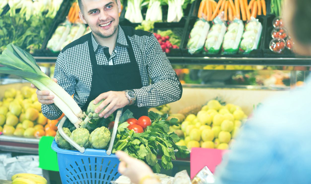 Man seller is assisting customer to buy fruit and vegetables in grocery shop.