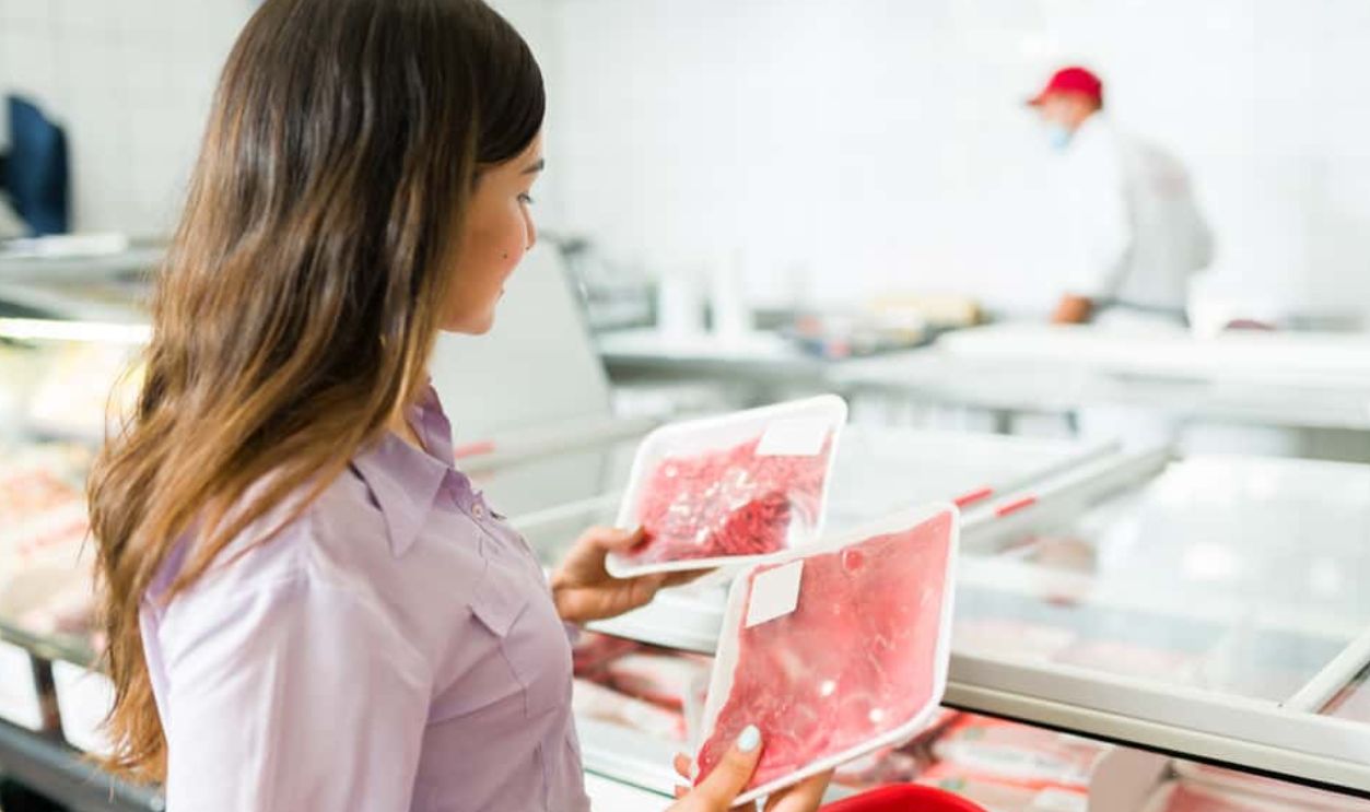 I want to buy something for dinner. Attractive woman seen from behind choosing raw meat or steak to buy at the supermarket