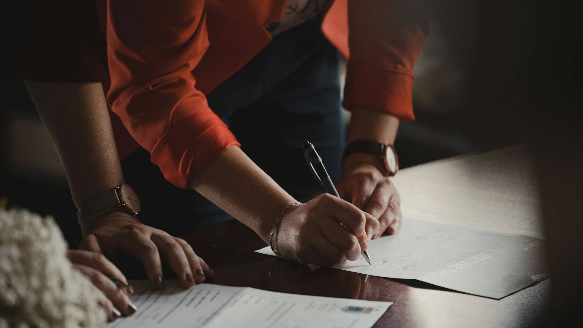 person in orange long sleeve shirt writing on white paper
