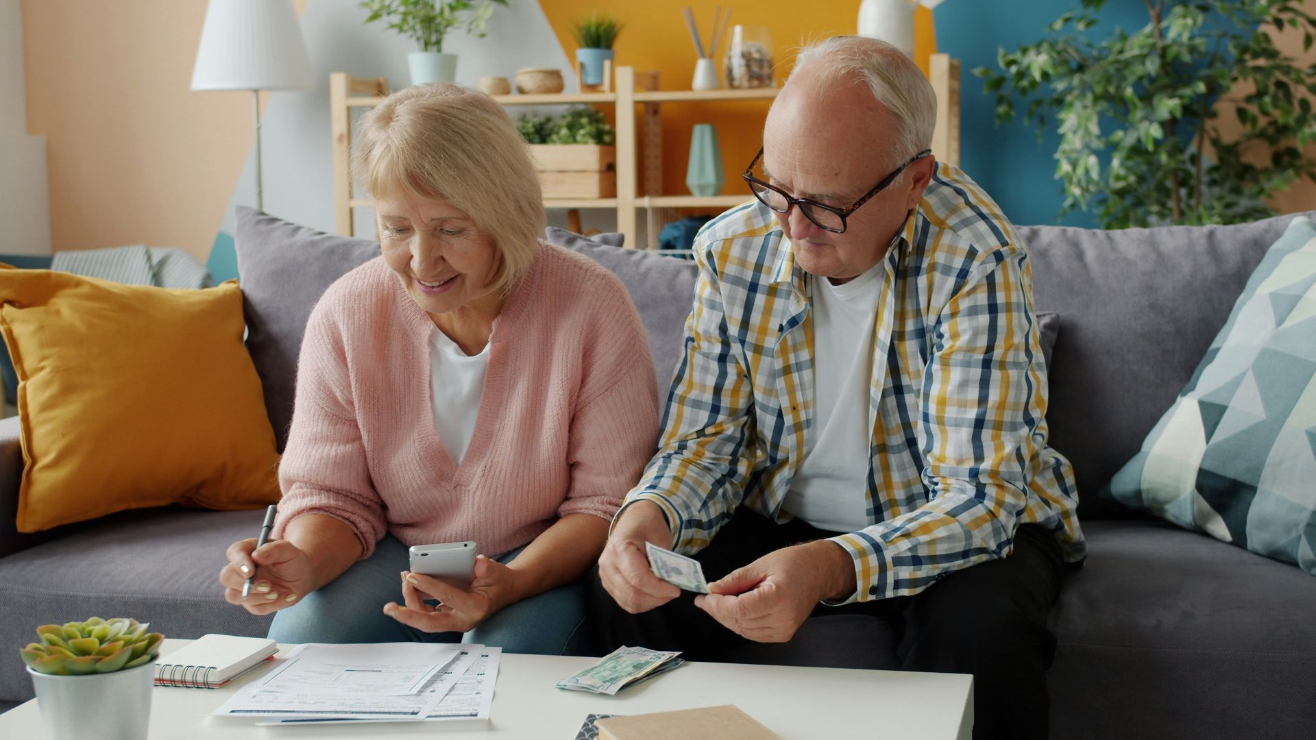 Elderly couple reviews finances at home on couch.
