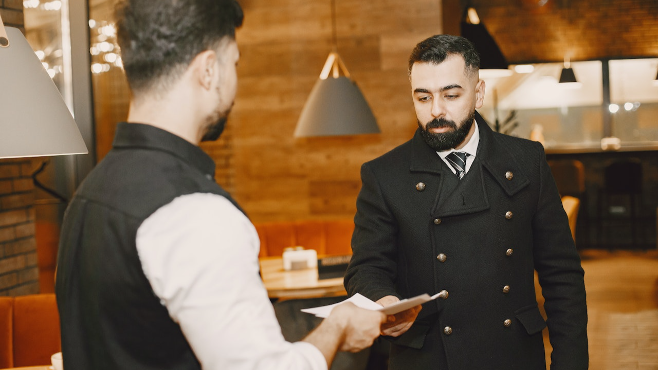 Man is giving a paper to a waiter at restaurant.