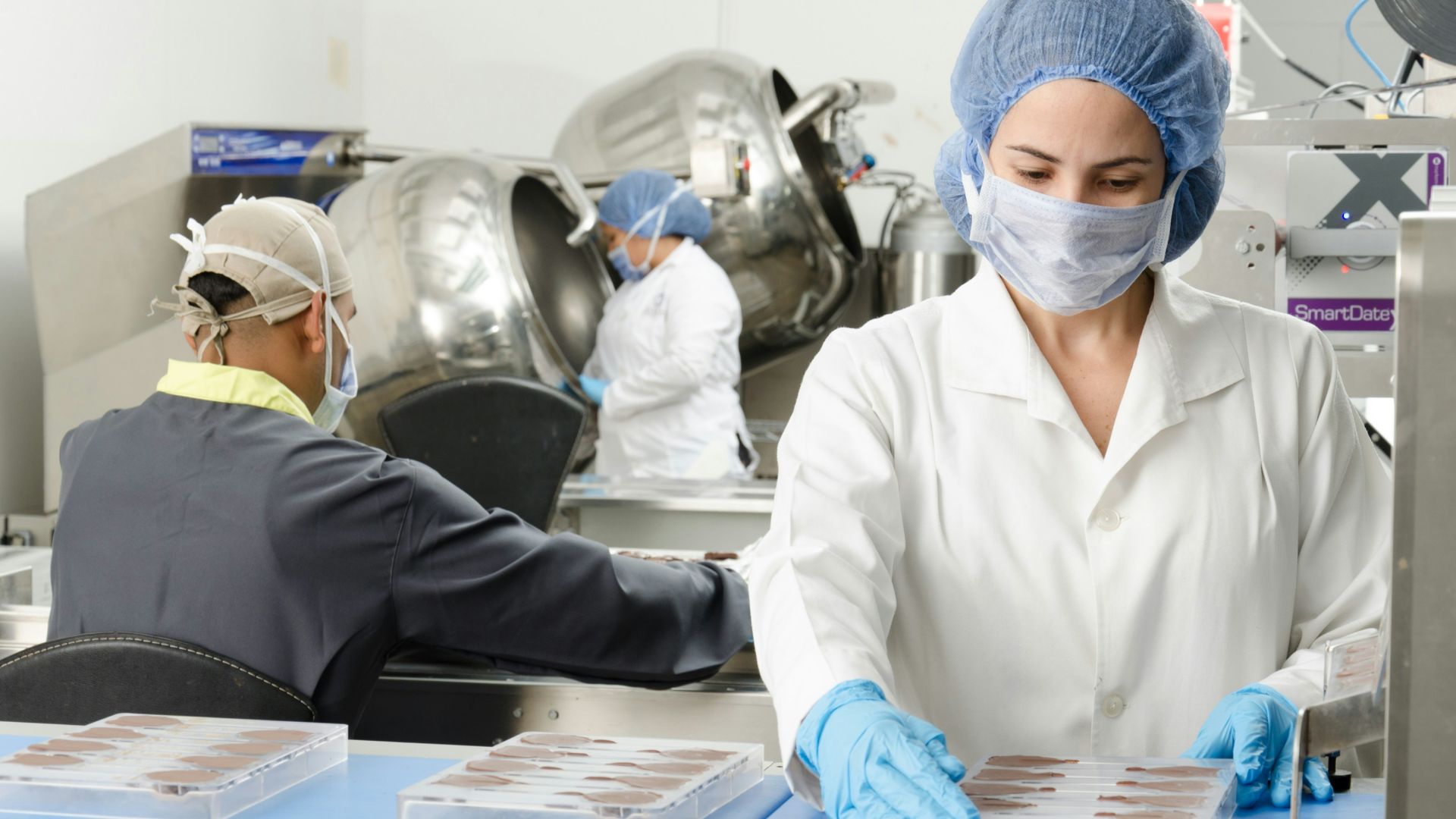 three people inside factory wearing masks and coats