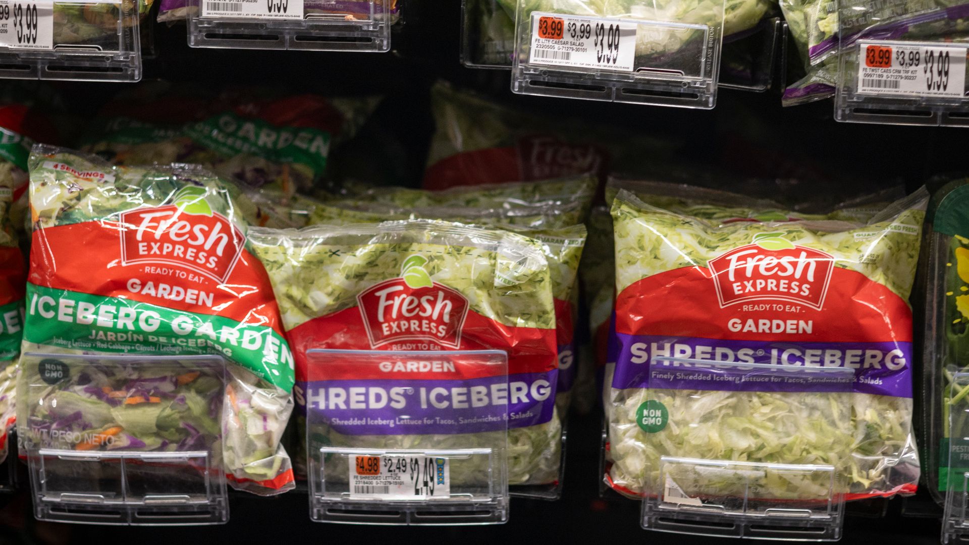 A refrigerated grocery display holds Fresh Express salad mixes and salad kits with price tags shown in clear plastic holders.