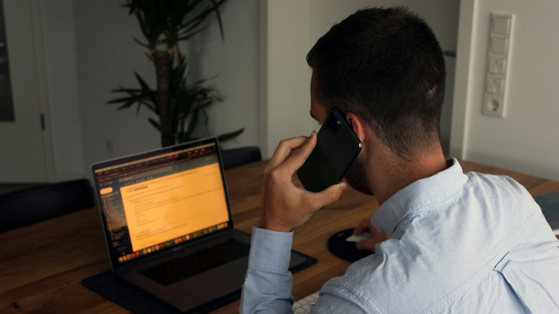 man in blue dress shirt holding black smartphone