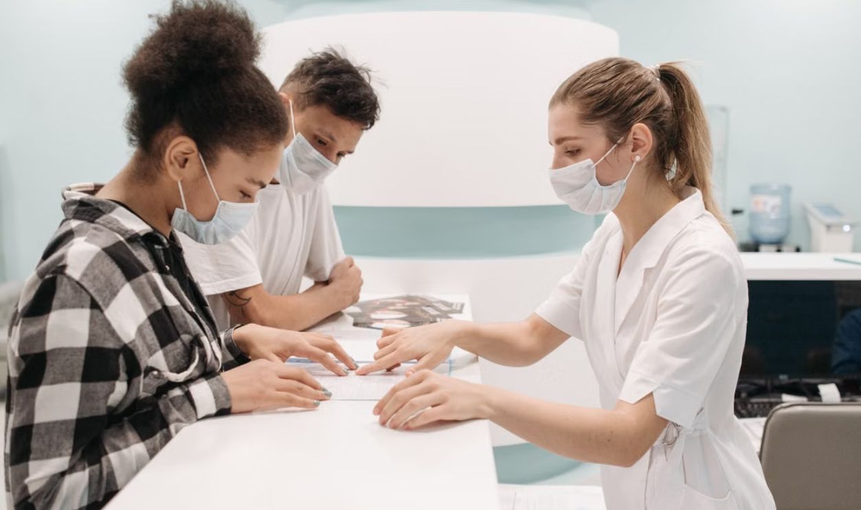 A healthcare professional in a medical setting assists patients at a clinic desk, emphasizing care and teamwork