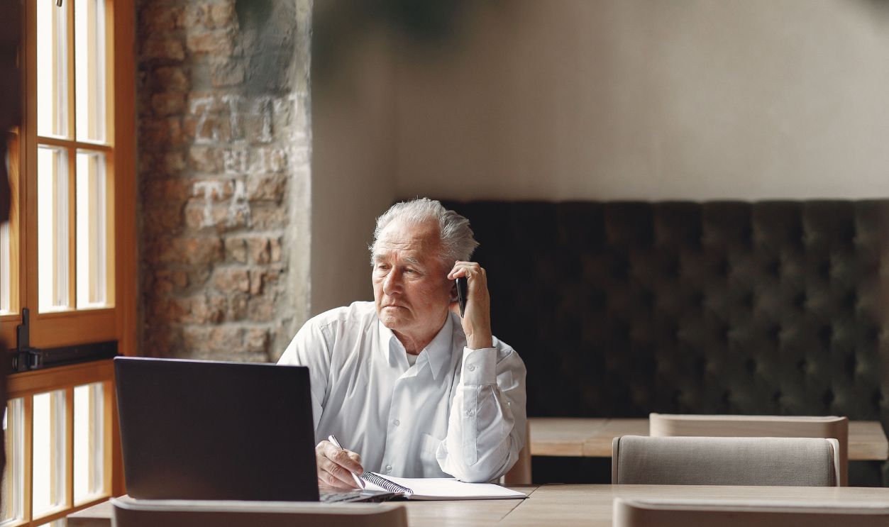 Senior businessman making a phone call while using a laptop in an office setting