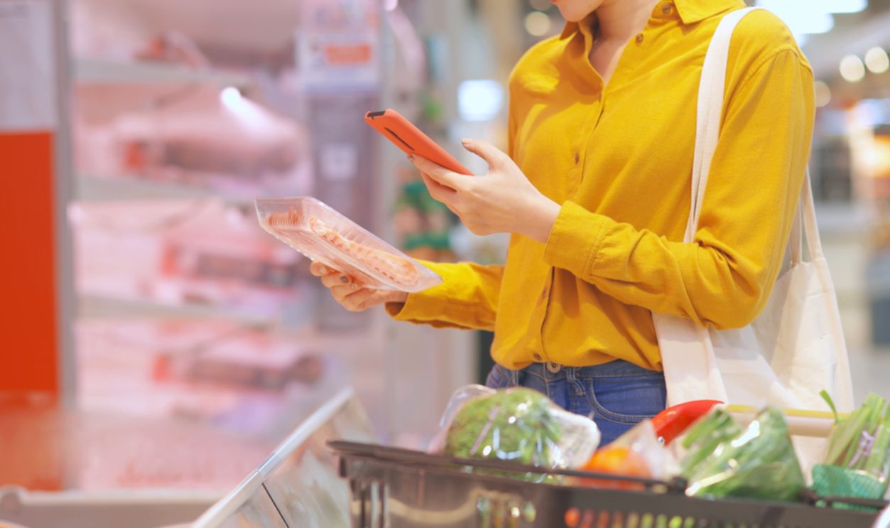 close up of asian young businesswoman is shopping for meat and scanning barcode with smart phone at supermarket