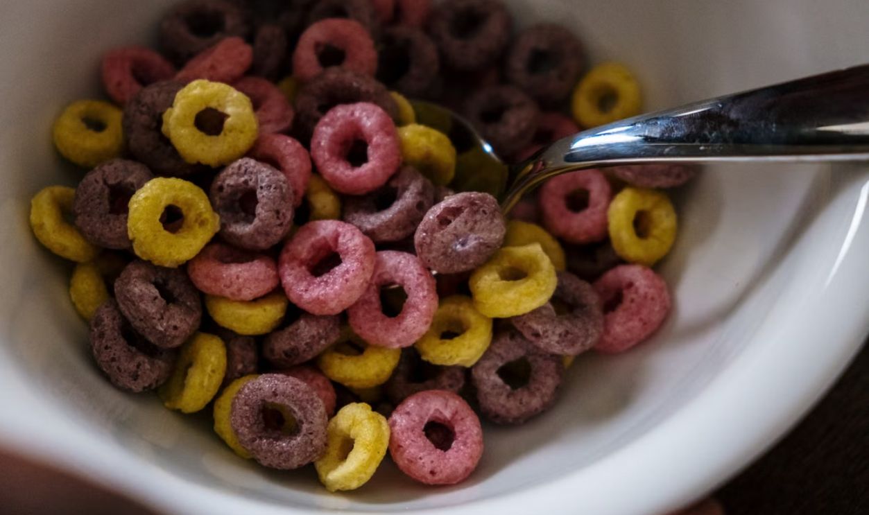 Vibrant fruity cereal rings in a white bowl with a spoon, emphasizing breakfast theme.