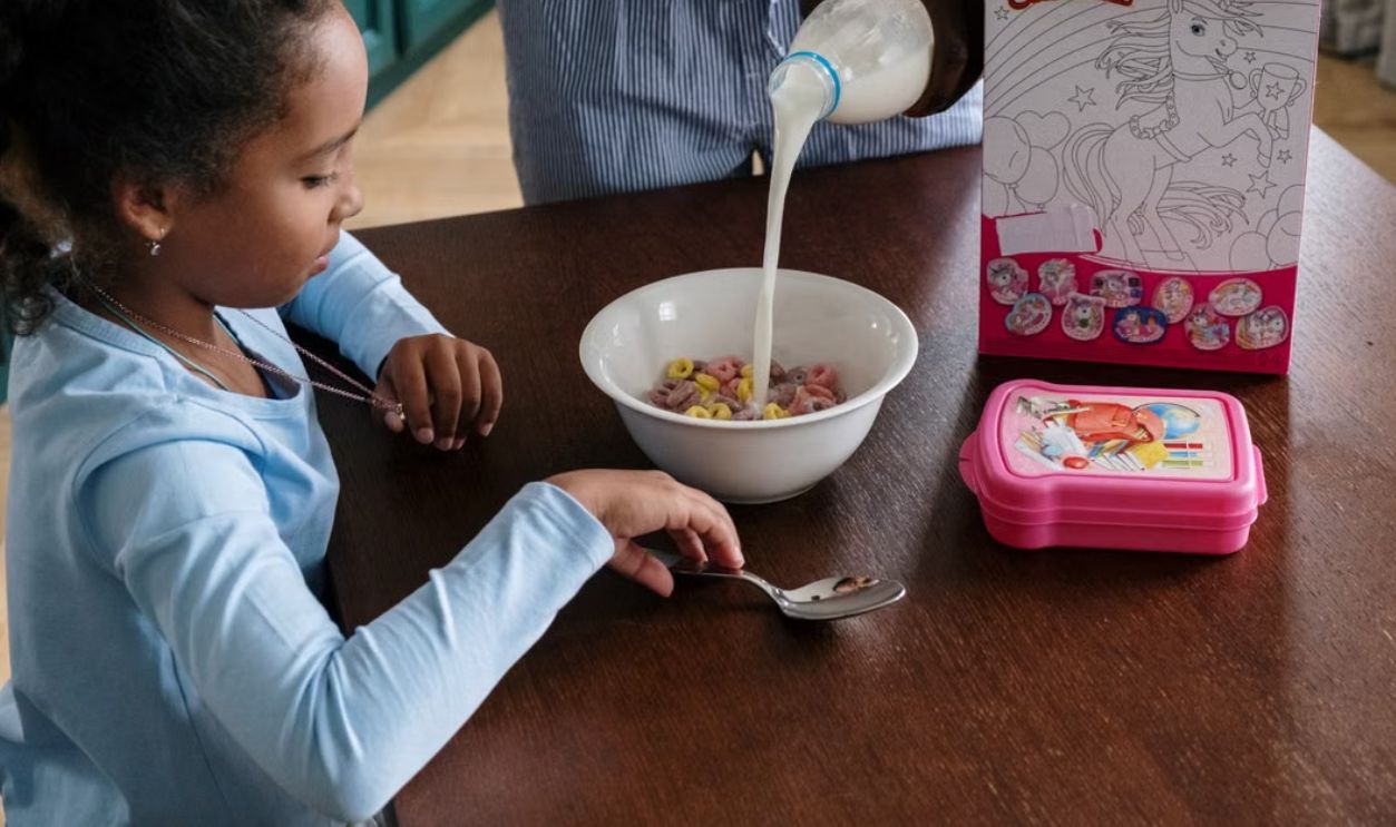 Young girl with cereal and milk at breakfast, captured indoors in a cozy setting.