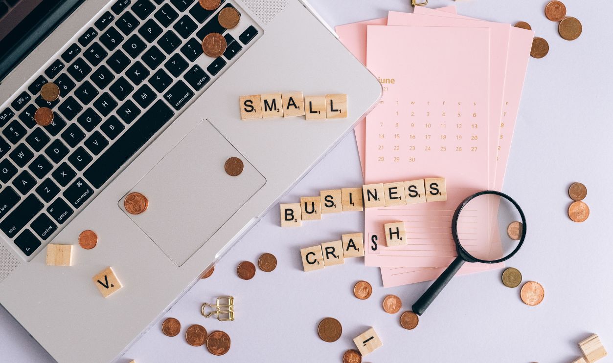 Flatlay of a laptop, coins, and scrabble tiles spelling 'small business crash'