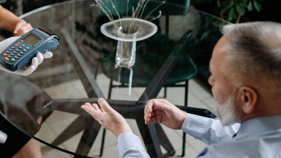 Senior couple completes payment with waiter in stylish restaurant setting, showcasing hospitality service.