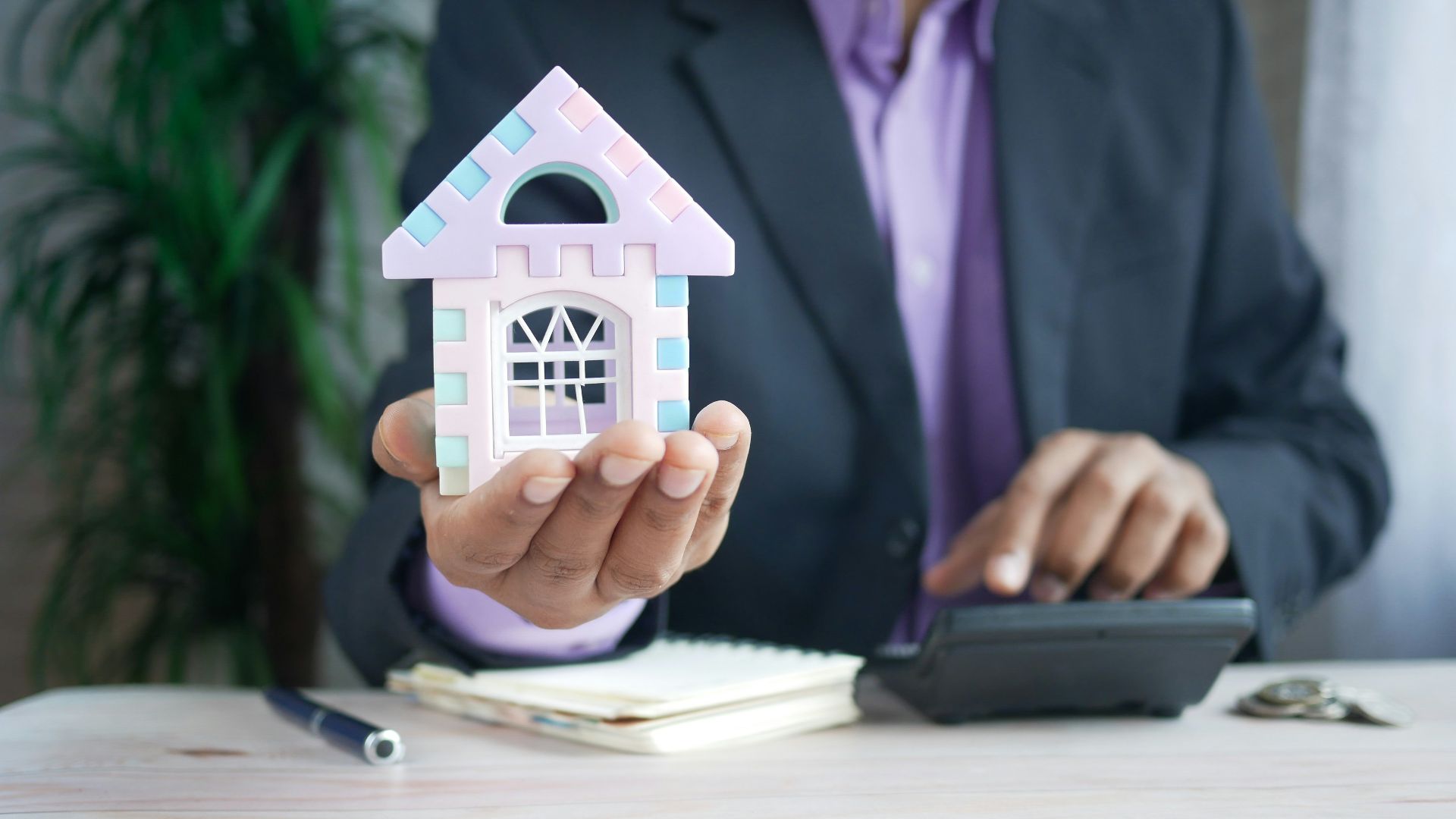 man holding model house at desk with calculator