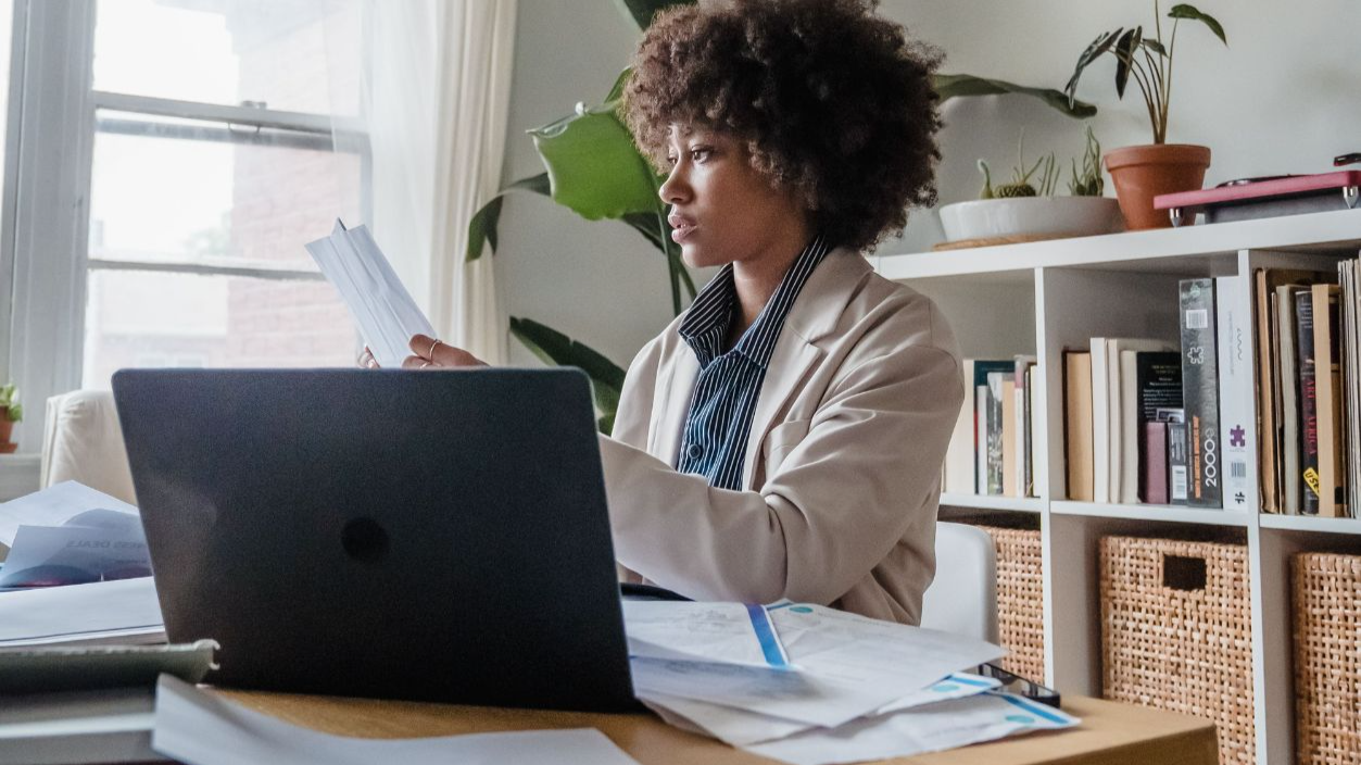 Woman working at a desk with laptop and papers, emphasizing remote work lifestyle