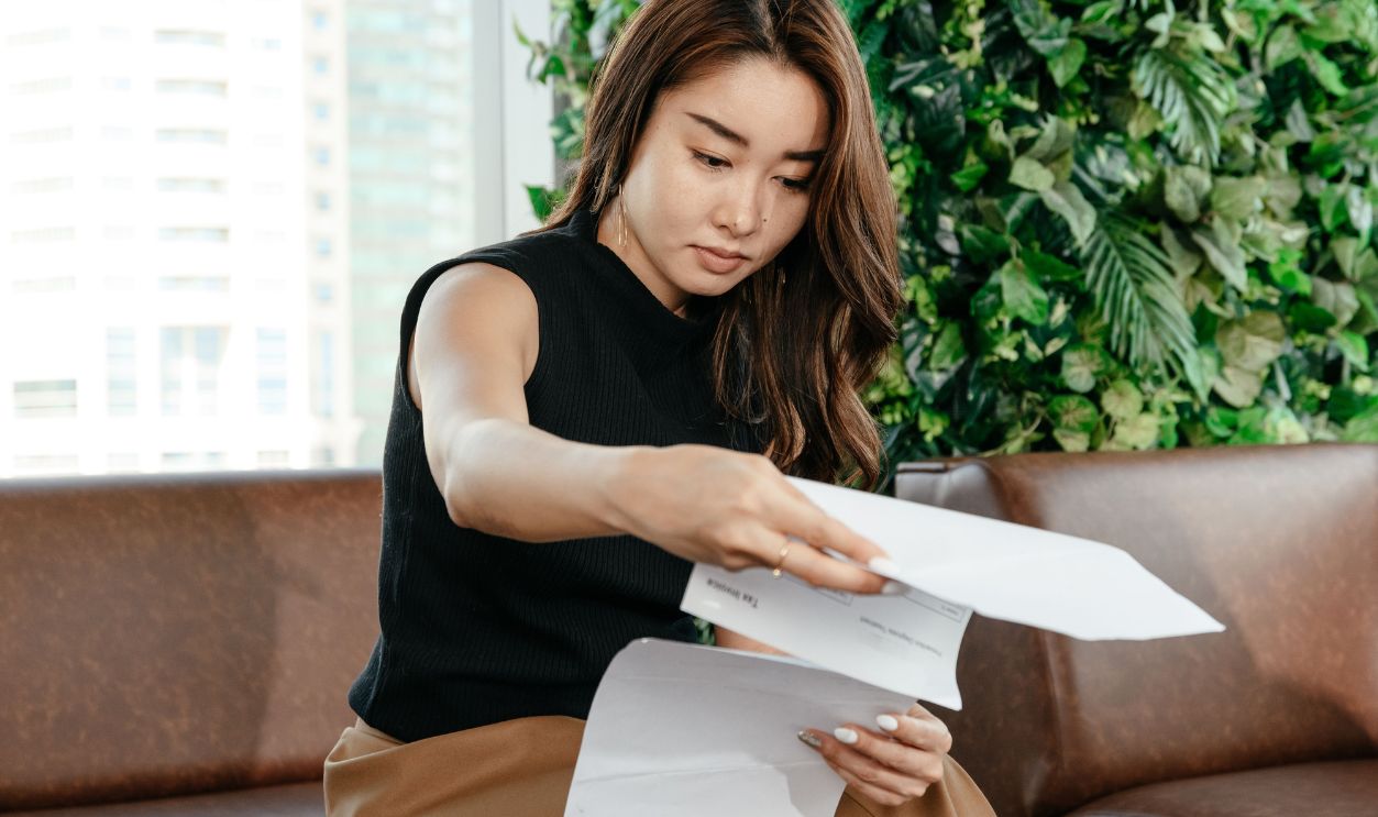 An Asian woman focusing on paperwork in a modern indoor workspace, showcasing professionalism and efficiency