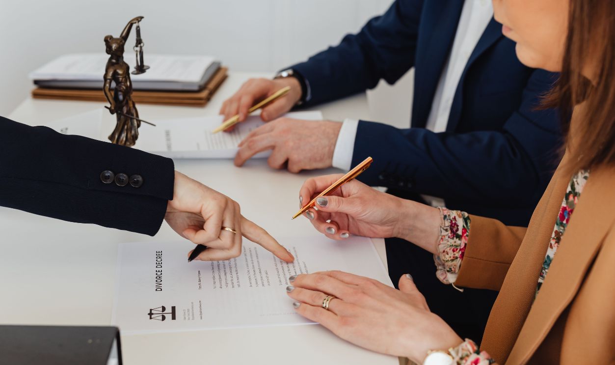 Hands signing a divorce decree, with a justice statue nearby, symbolizing legal proceedings.