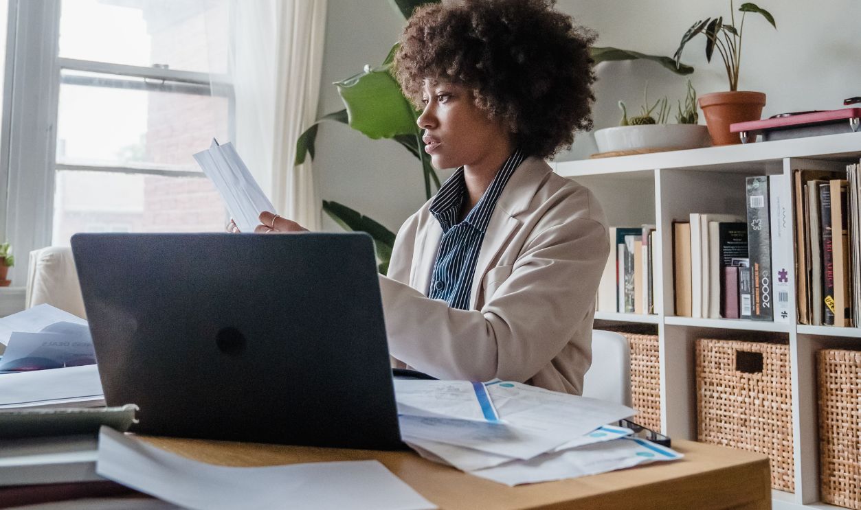 Woman working at a desk with laptop and papers, emphasizing remote work lifestyle