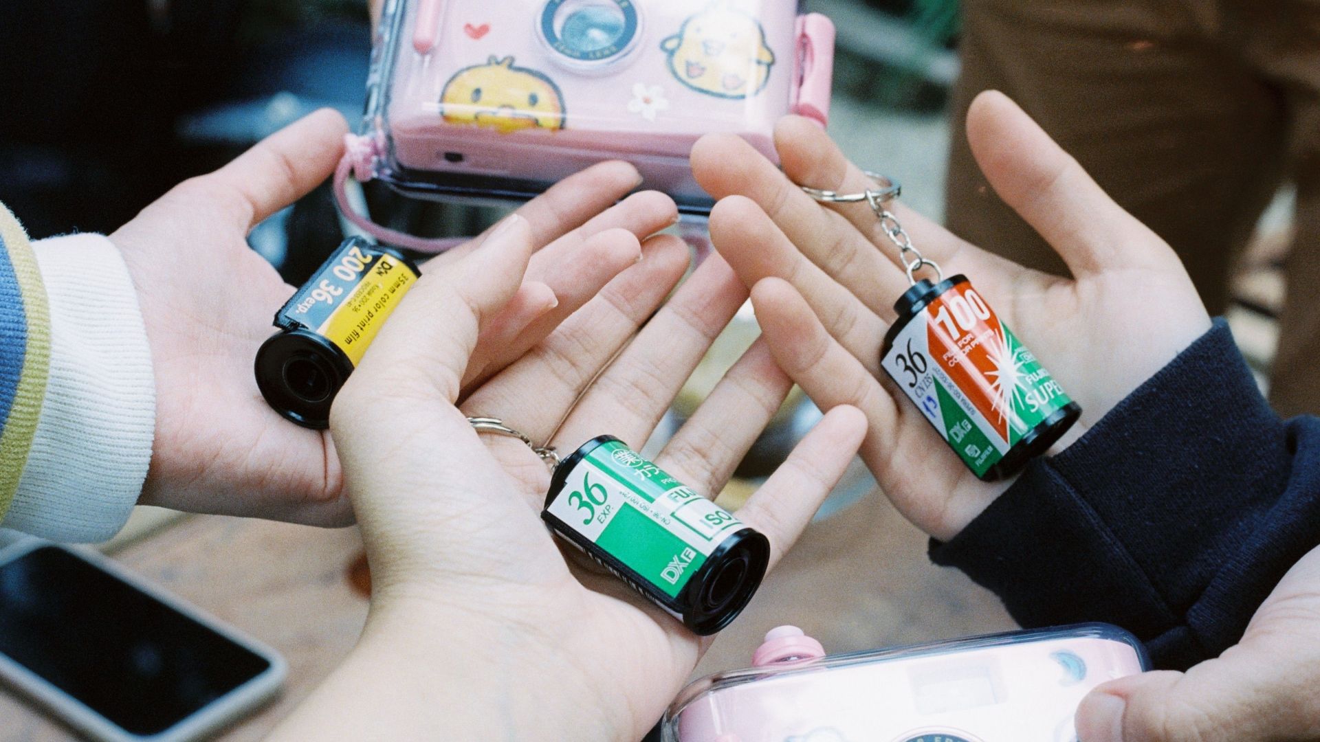 A close-up of hands holding various film roll keychains with a playful camera case.