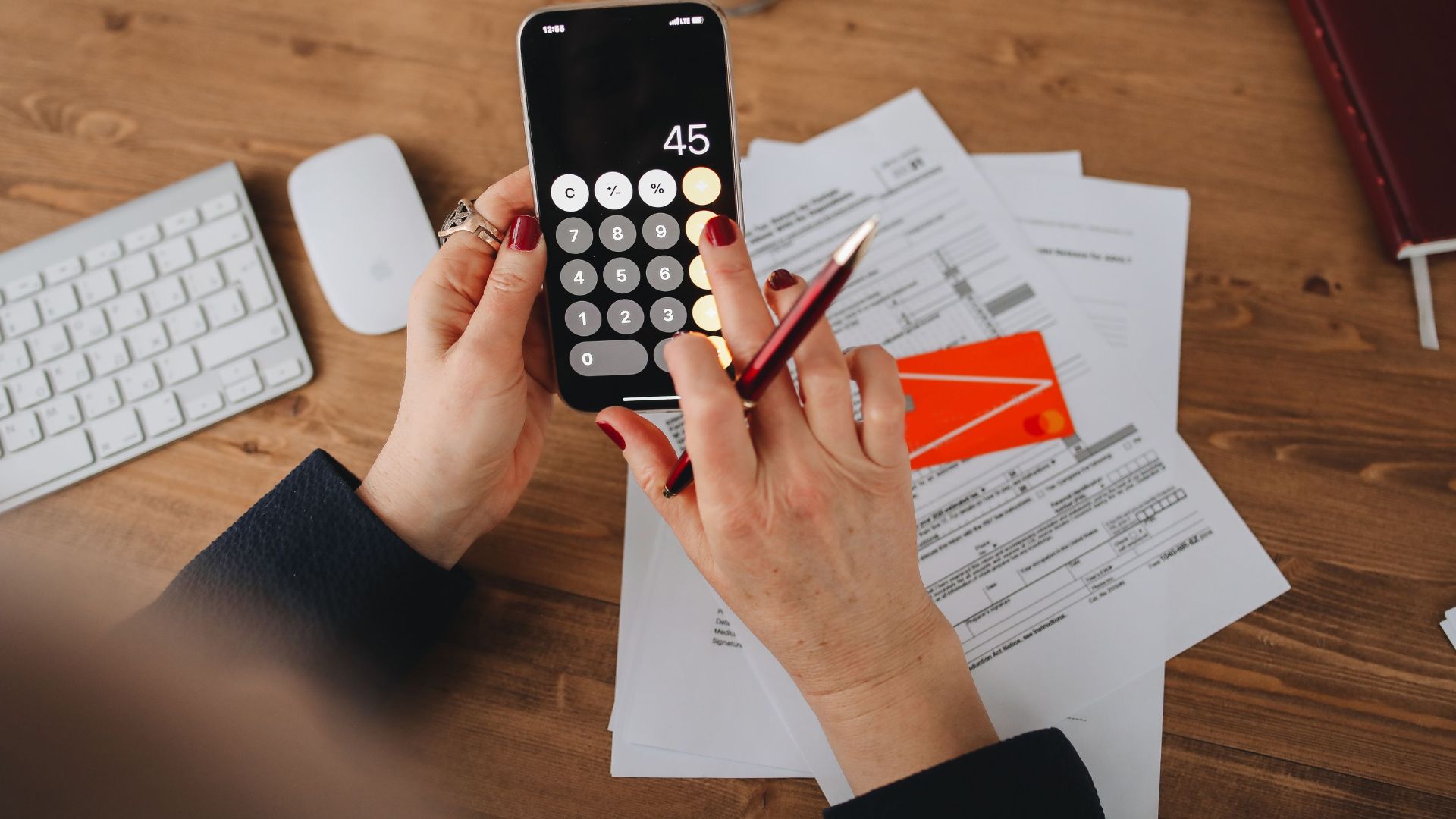 Hands using a calculator app on a smartphone over financial documents. Perfect for illustrating finance or technology themes.