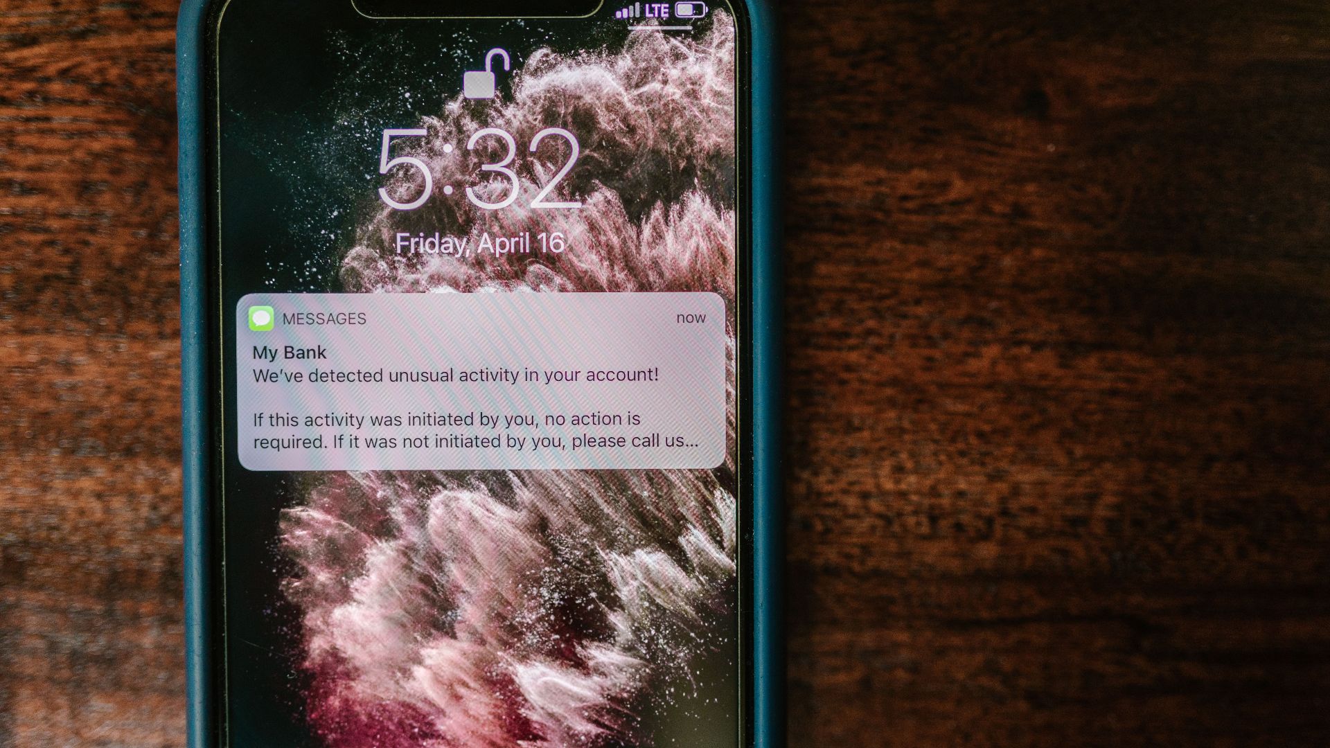 Close-up of a smartphone displaying a bank alert notification on a wooden table.