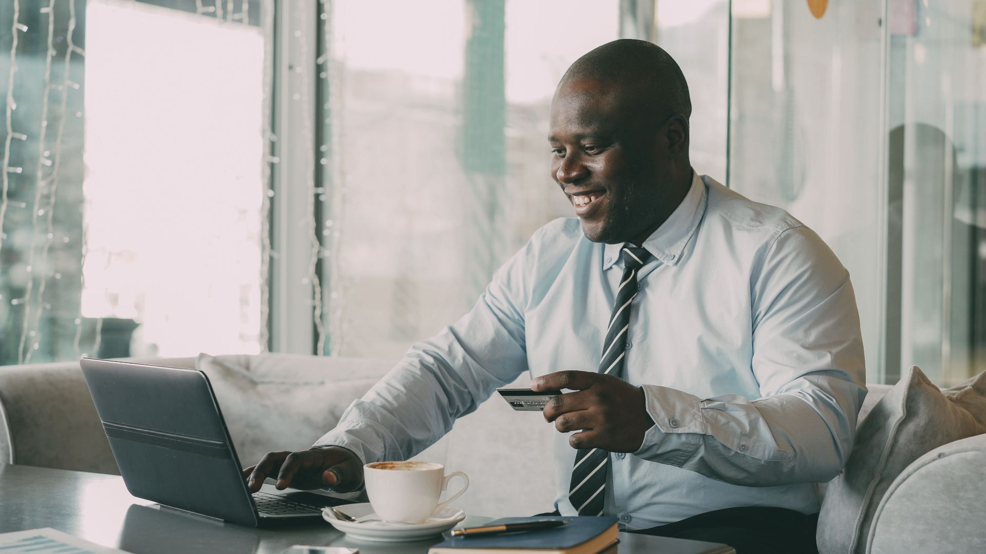 Smiling businessman using tablet and credit card in a cafe.