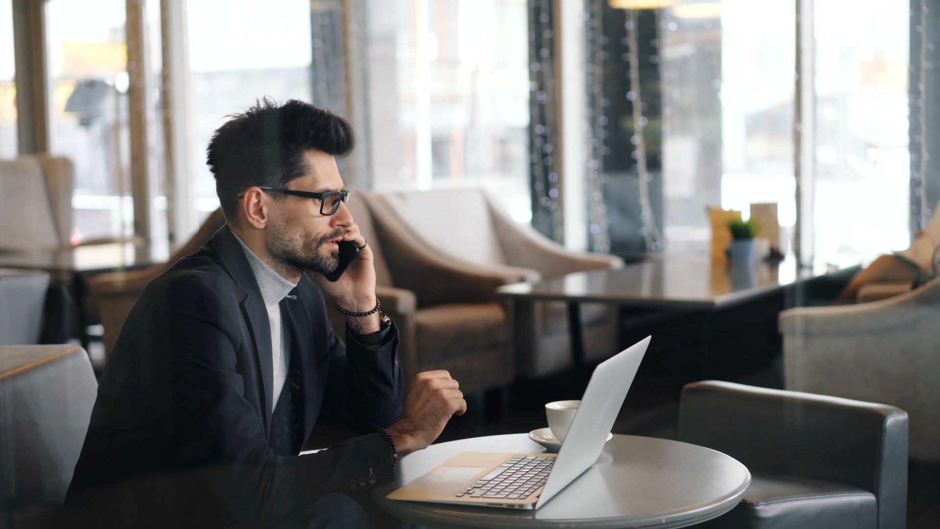 Business professional using smartphone and laptop in a café for a remote work meeting.