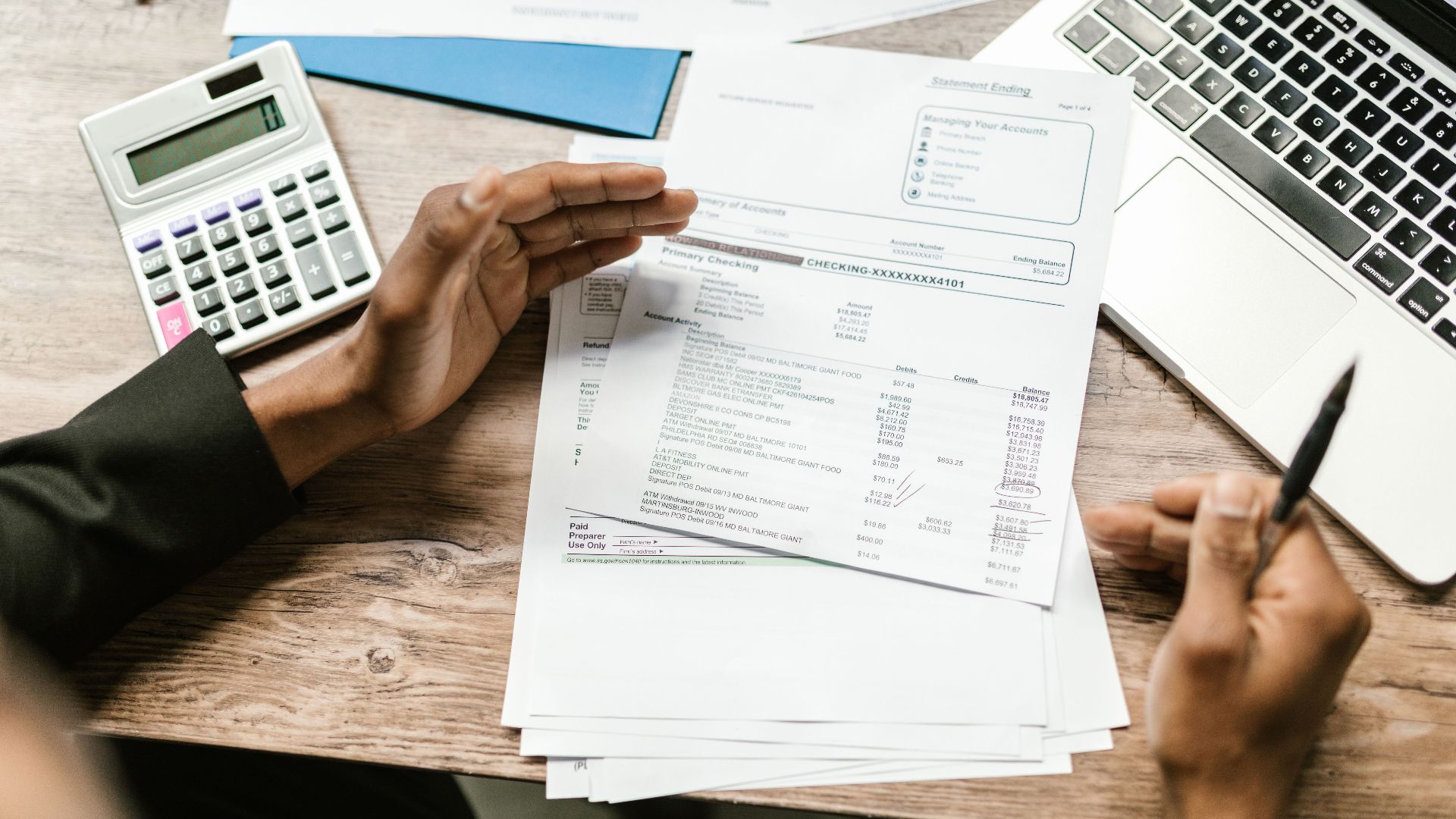 Hands holding financial documents with calculator and laptop on office desk, business analysis scene.
