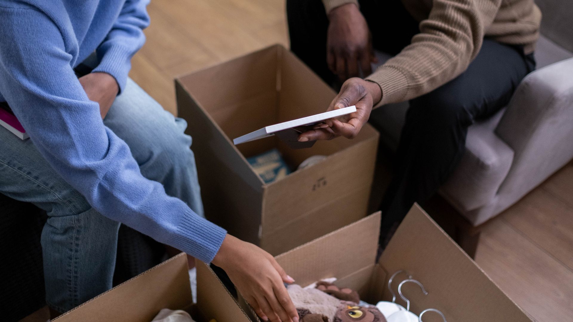 A couple sorts through boxes, packing and organizing household items together indoors.