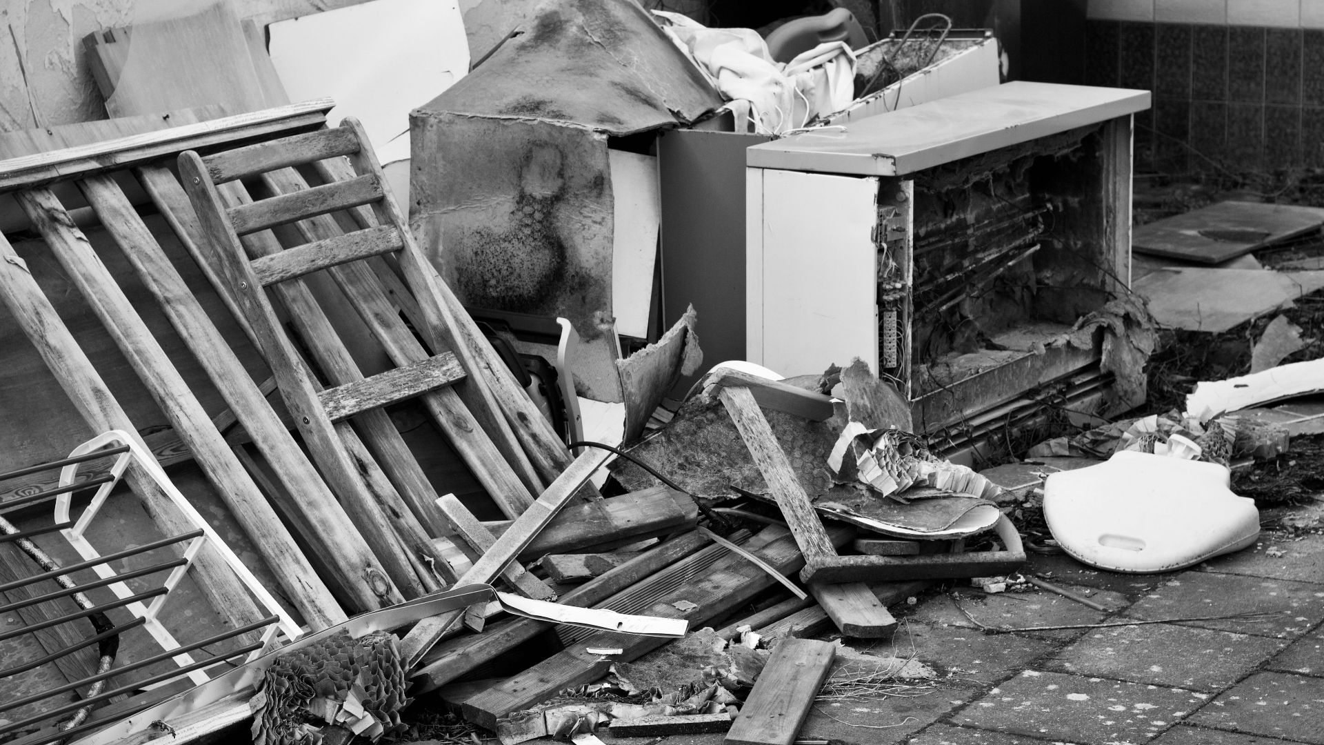 Black and white image of a pile of discarded objects in an urban setting, highlighting decay.
