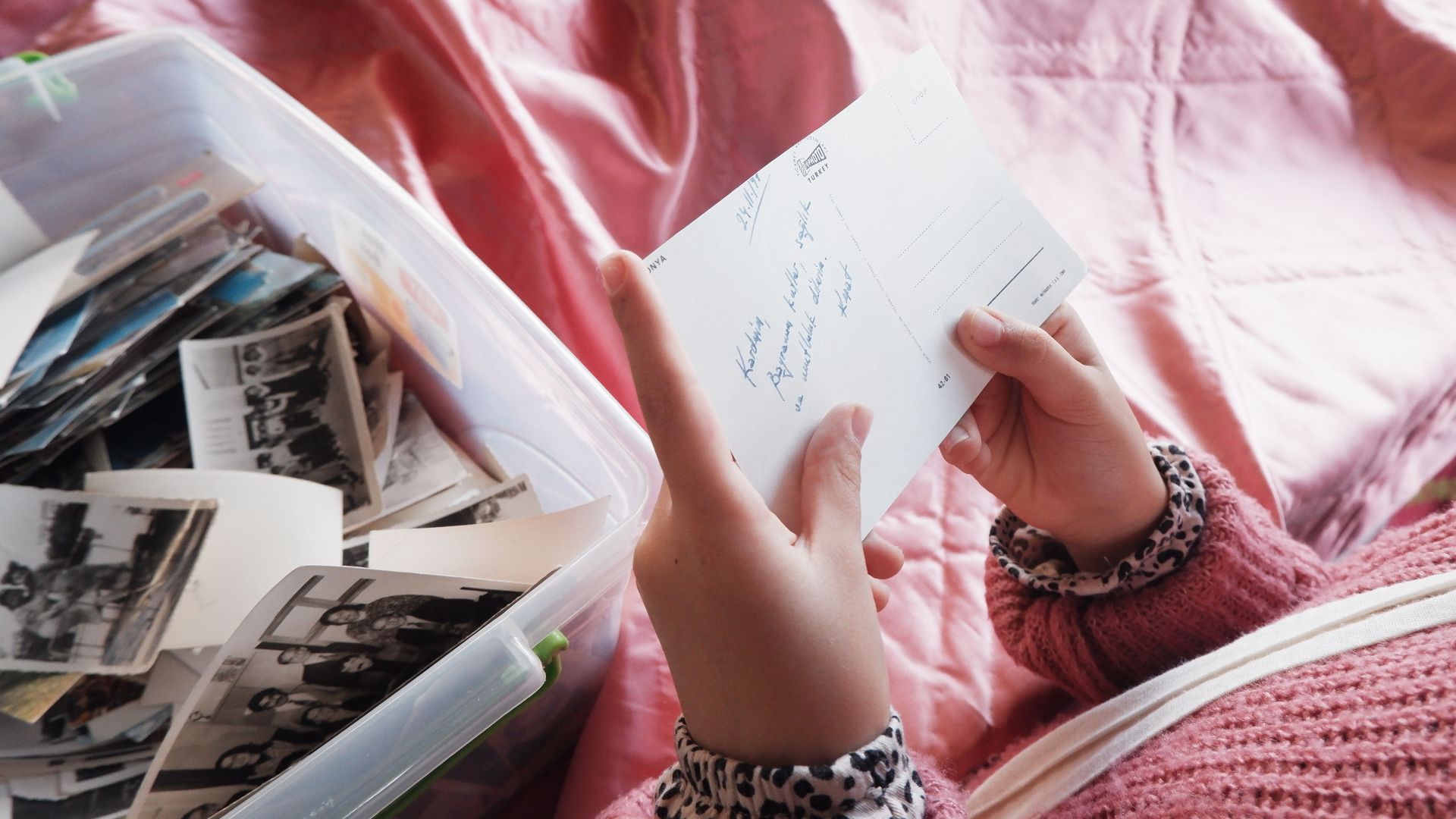Close-up of a woman holding a postcard, exploring memories from a photo box.