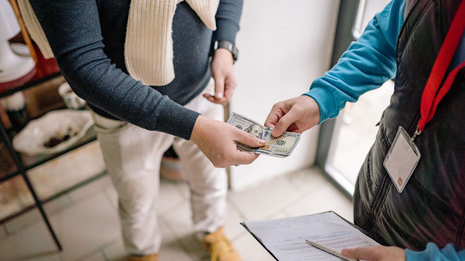 Close-up of hands exchanging cash during a transaction indoors, highlighting payment details.