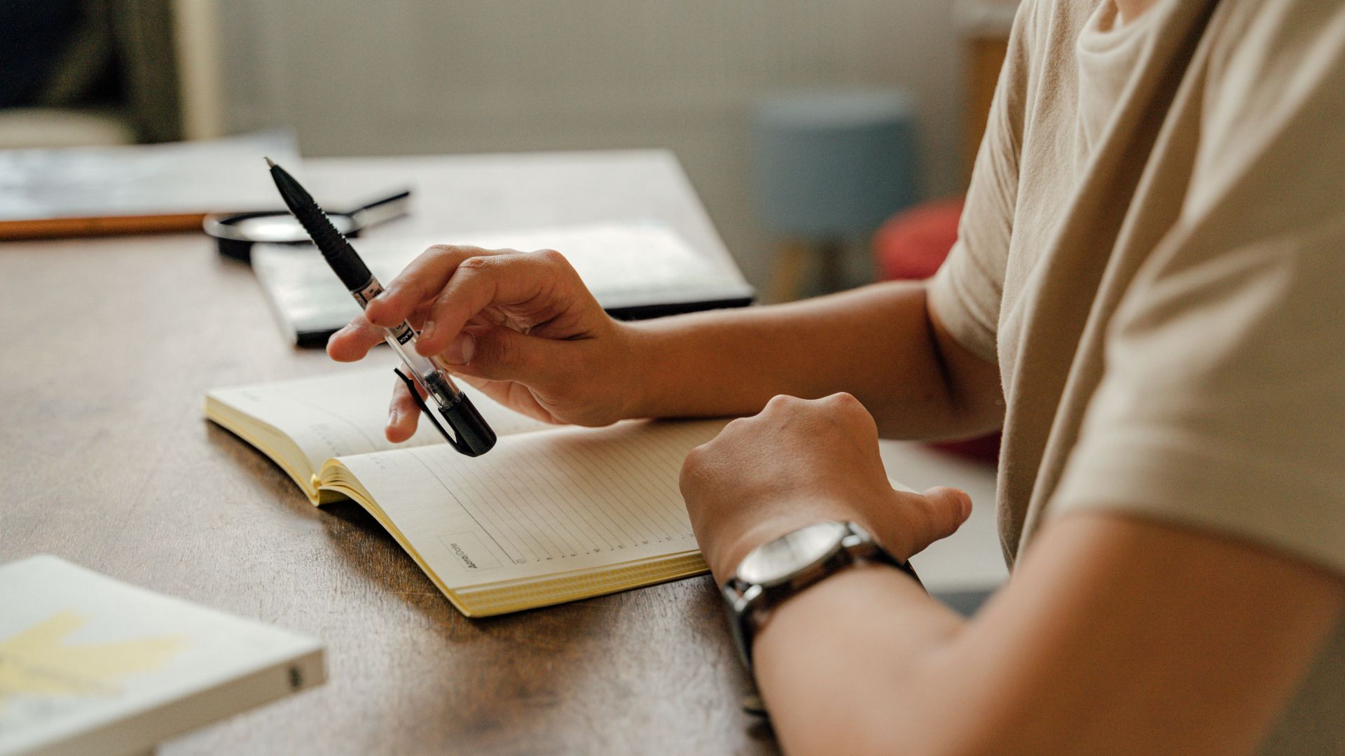 A person writing with a pen in a notebook on a wooden desk, indoors.