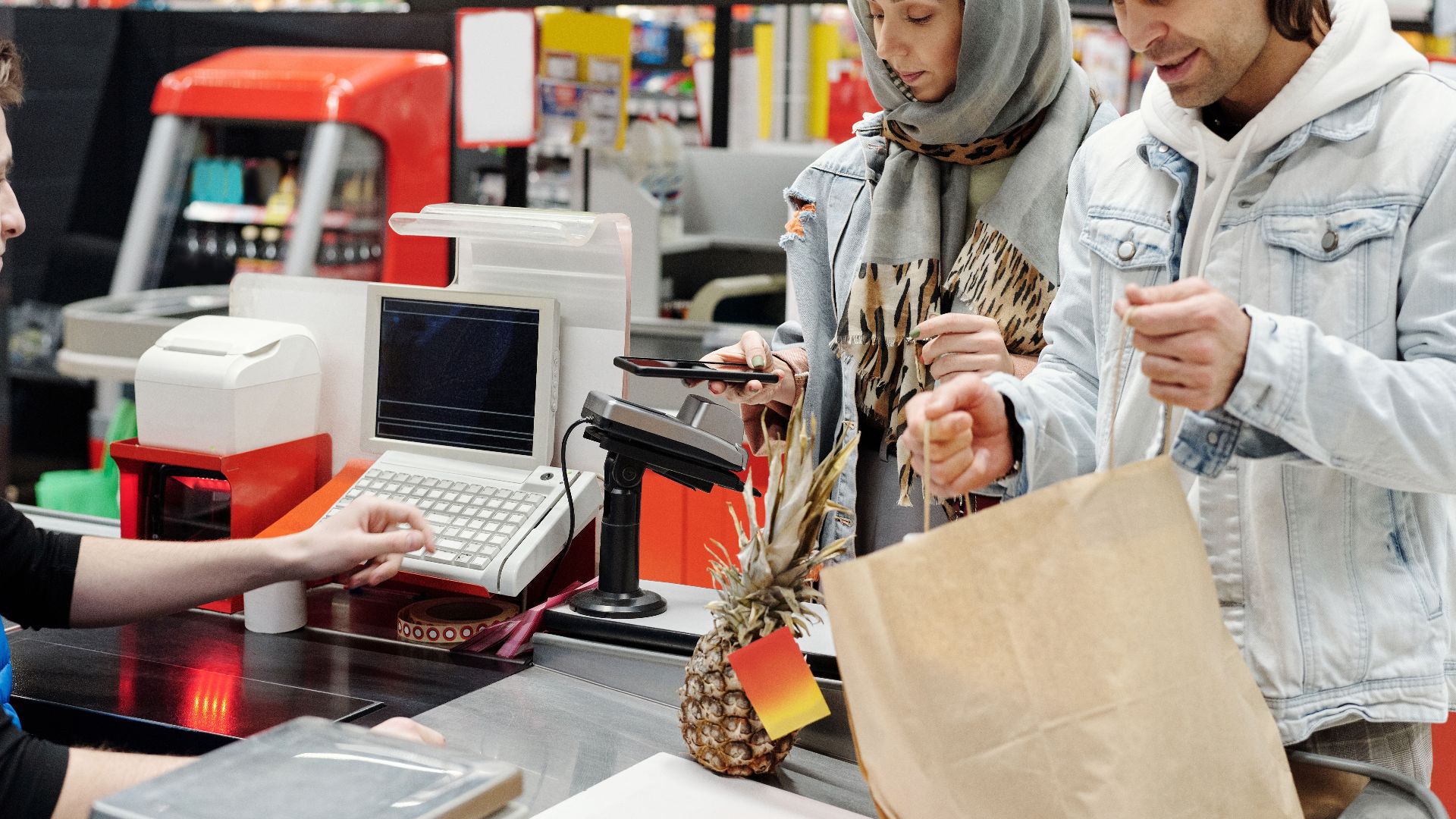 A Middle Eastern couple making a purchase at a supermarket checkout using a smartphone.